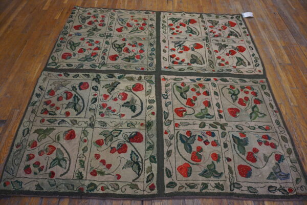 Hooked rug featuring red strawberry motifs and green vines in framed panels on hardwood flooring.