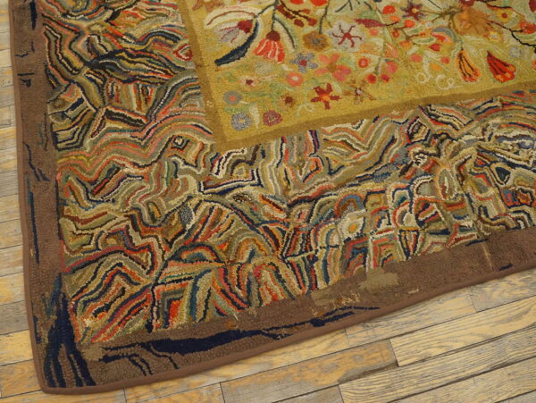 Textured hooked rug with an olive floral center and a wavy, multicolored abstract border on wood flooring.