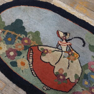 Hooked oval rug with a central female figure, red dress, and multicolored floral border on distressed wood floor.