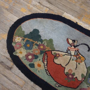 Oval rug with hooked texture showing a figure and multicolor flowers on weathered gray wood floor.