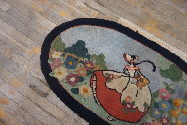 Oval rug with hooked texture showing a figure and multicolor flowers on weathered gray wood floor.