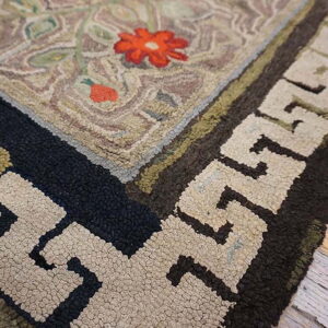 The rug corner features a textured beige field with red flowers and a dark geometric meander border on a wood floor.