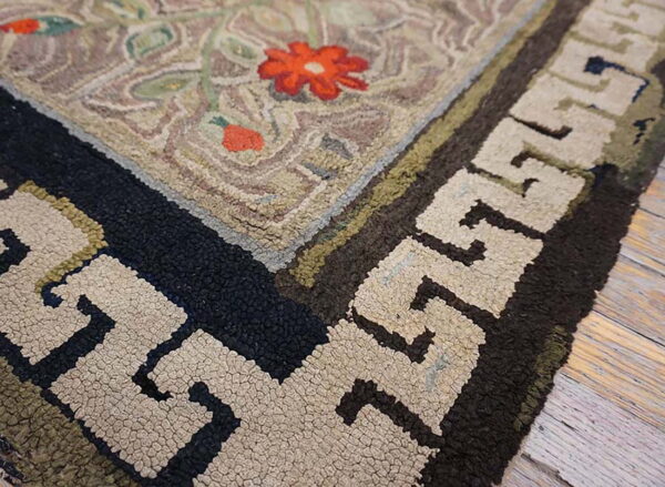 The rug corner features a textured beige field with red flowers and a dark geometric meander border on a wood floor.