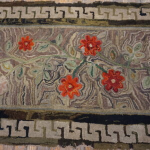 Textured rug with red floral motifs and a Greek key border lies across light wood flooring.