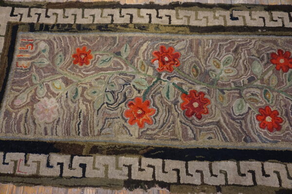 Textured rug with red floral motifs and a greek key border lies across light wood flooring.
