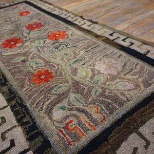 A hooked runner rug featuring red flowers, green vines, and a Greek key border on wood floor.