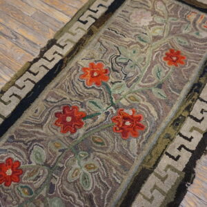 Rustic runner with bright red flowers, green vines, and a taupe Greek key border on wood flooring.