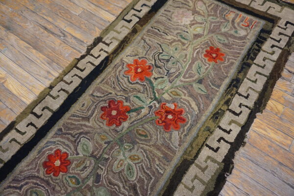 Rustic runner with bright red flowers, green vines, and a taupe greek key border on wood flooring.
