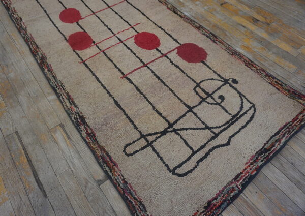 Low-pile runner rug with a beige field, black lines, and red circular motifs, resting on gray wood flooring.