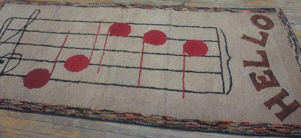 Beige textured rug displaying a black musical staff, red notes, and the word hello on wood floors.