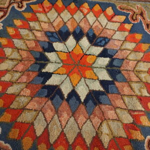 Textured rug with a multicolored starburst pattern made of diamonds and a scrolled outer border.