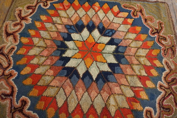Textured rug with a multicolored starburst pattern made of diamonds and a scrolled outer border.