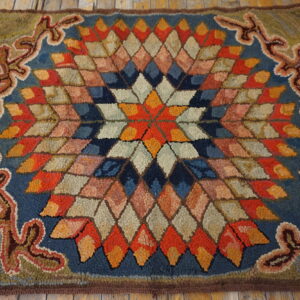 Textured rug with a colorful diamond starburst center and green patterned border resting on wood planks.