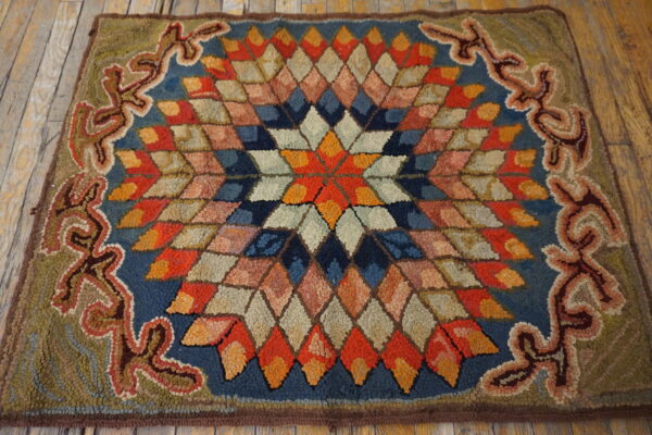 Textured rug with a colorful diamond starburst center and green patterned border resting on wood planks.