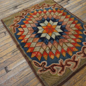 Multicolored hooked rug featuring a geometric star center and scroll border on a distressed wood floor.