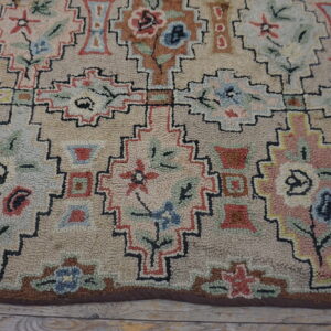 A looped pile rug displaying muted geometric floral patterns rests on distressed light wood floorboards.