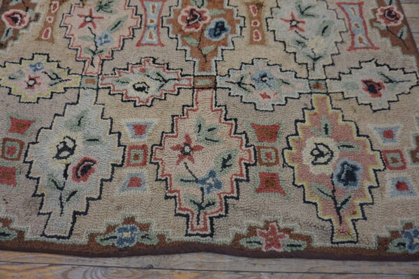 A looped pile rug displaying muted geometric floral patterns rests on distressed light wood floorboards.