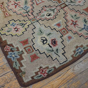 Muted beige rug with multicolor geometric floral designs and looped texture lies on distressed wood planks.