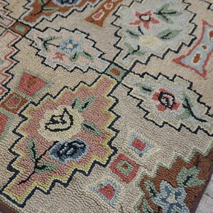 Muted floral and geometric hooked rug with pink and blue details, visible on distressed wood flooring.