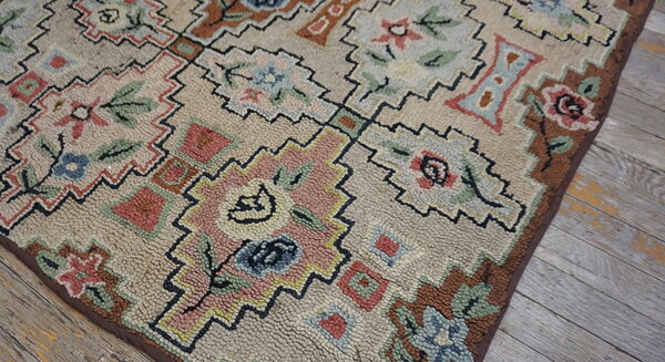 Muted floral and geometric hooked rug with pink and blue details, visible on distressed wood flooring.
