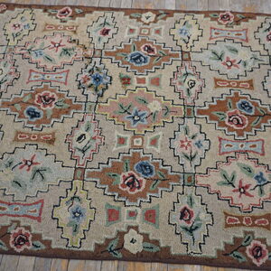 Beige rug with multicolored geometric and stylized floral motifs in brown, blue, and pink on plank wood flooring.