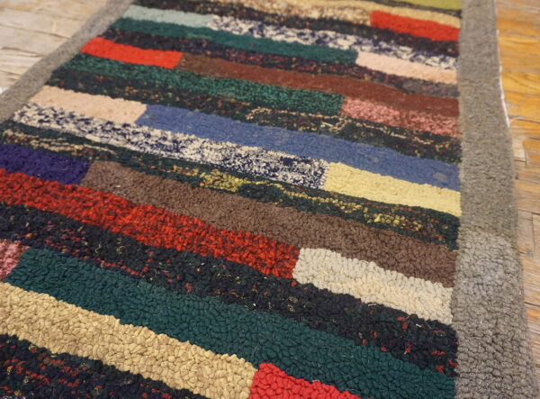 A close-up shows a chunky, multicolored striped rug with a thick gray border on a wooden floor.