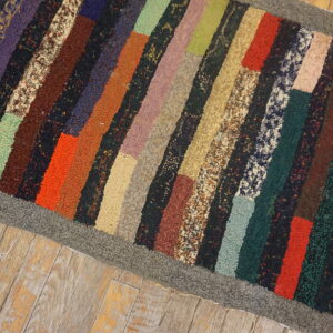 Highly textured multicolor striped rug with a gray border placed on distressed wooden plank flooring.