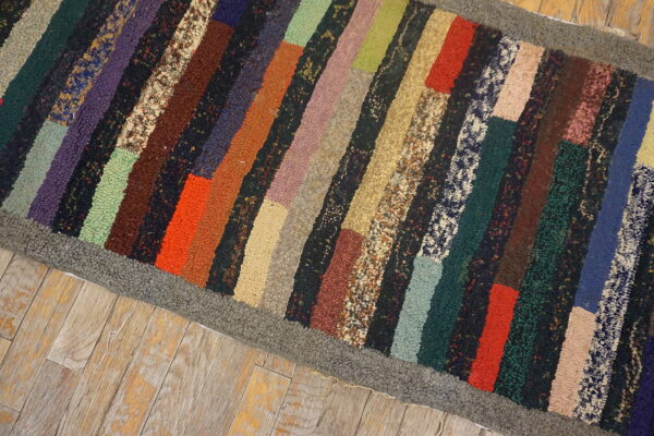 Highly textured multicolor striped rug with a gray border placed on distressed wooden plank flooring.