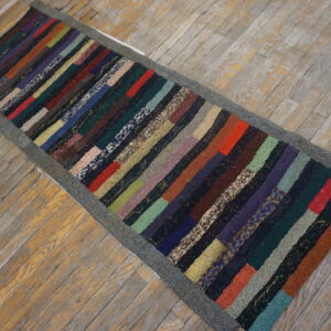 Multicolored striped runner rug with a dark gray border lies on worn light wood plank flooring.