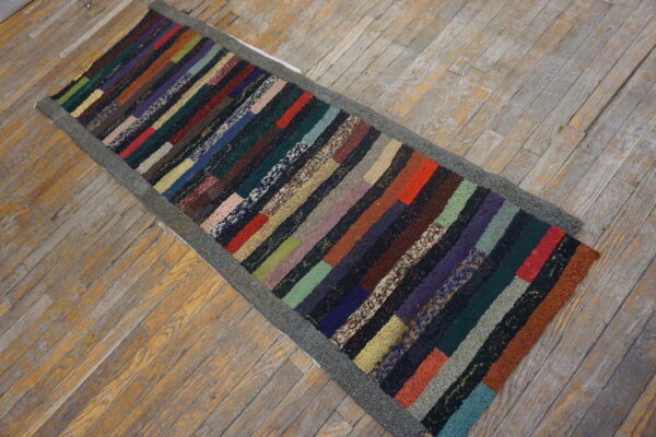 Multicolored striped runner rug with a dark gray border lies on worn light wood plank flooring.