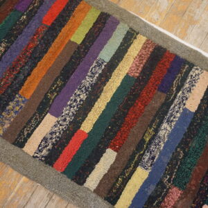 Highly textured, multi-colored hooked runner with variegated patches and a gray border on distressed wood.