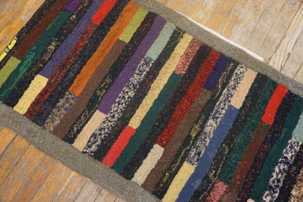 Highly textured, multi-colored hooked runner with variegated patches and a gray border on distressed wood.
