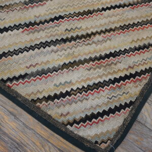 Textured rug featuring multi-colored zig-zag stripes and a dark green binding sits on weathered wood flooring.