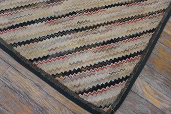 Textured rug featuring multi-colored zig-zag stripes and a dark green binding sits on weathered wood flooring.