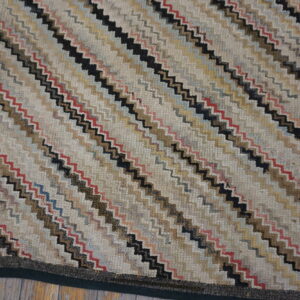Multicolored, textured low-pile rug with diagonal zigzag stripes in cream, black, brown, and red resting on wood flooring.