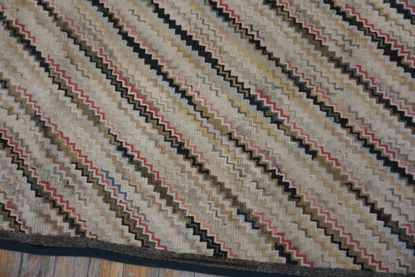 Multicolored, textured low-pile rug with diagonal zigzag stripes in cream, black, brown, and red resting on wood flooring.