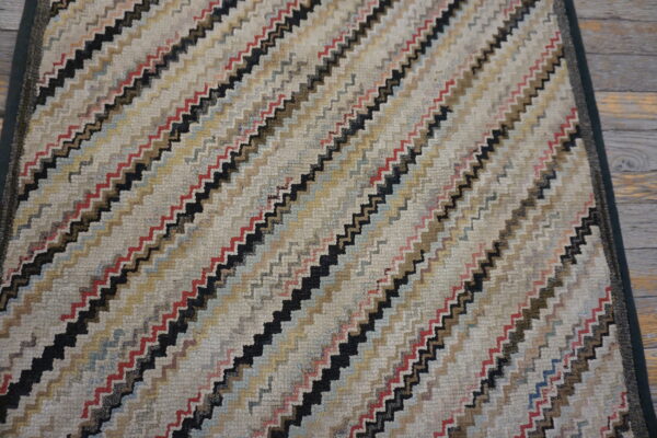 Textured rug with multicolored zigzag diagonal stripes, including red and black, displayed on wooden planks.