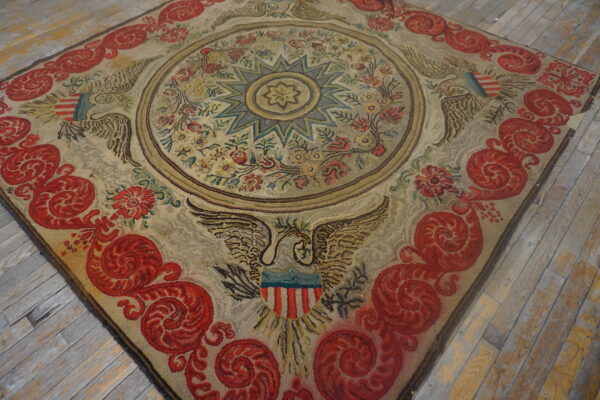 Beige rug with red scrolling borders and eagle motifs rests on worn wood flooring.