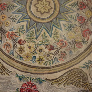 Hooked pile rug with a faded look, showing floral garlands, a star center, and an eagle motif.