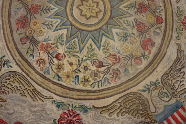 Hooked pile rug with a faded look, showing floral garlands, a star center, and an eagle motif.