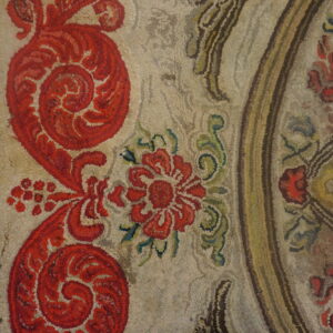 A highly textured rug features large red floral motifs on a neutral tan ground next to light distressed wood.