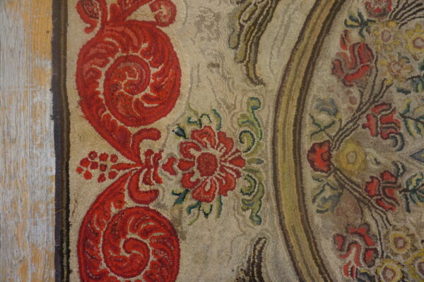 A highly textured rug features large red floral motifs on a neutral tan ground next to light distressed wood.