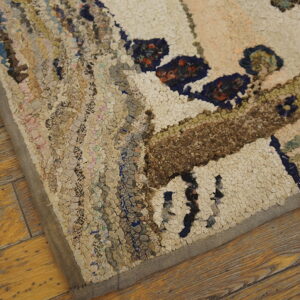 Highly textured hooked rug featuring cream, blue, and brown patterns, viewed close-up on wood flooring.