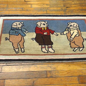 A low-pile rug showing three colorful dressed pigs on a blue background, placed on wood flooring.