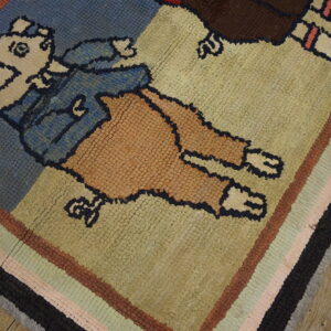 Blue, tan, and brown figural hooked rug with a striped border resting on light wood planks.
