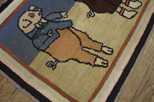 Blue, tan, and brown figural hooked rug with a striped border resting on light wood planks.