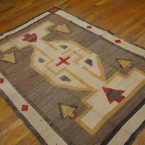 Flat-woven rug in brown, cream, yellow, and red geometric patterns resting on polished hardwood planks.