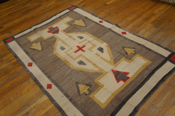 Flat-woven rug in brown, cream, yellow, and red geometric patterns resting on polished hardwood planks.