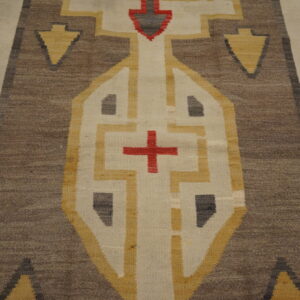 Brown flatwoven rug with gold and cream geometric patterns and red cross accent on wood floor.