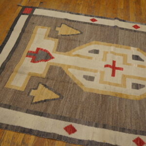 Brown, cream, and gold geometric rug with red motifs lying on distressed wooden floors.
